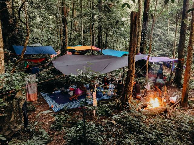 Camp with hammocks and tarps around a fire in the rainforest of Khao Sok